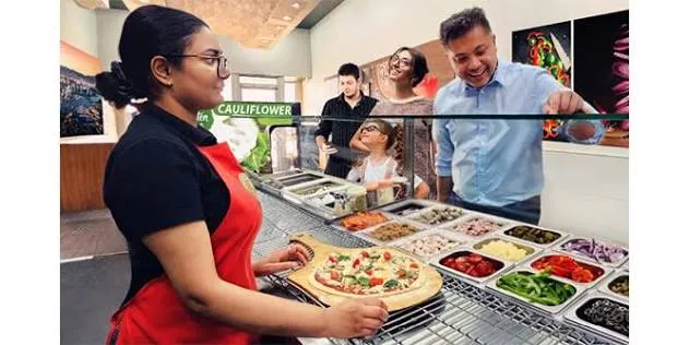 Freshslice Pizza employee preparing a customized pizza for customers